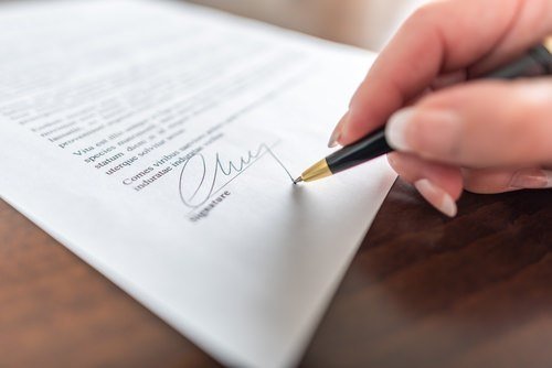 Primer plano de una mano sosteniendo un bolígrafo mientras firma un acuerdo de arbitraje sobre una mesa de madera