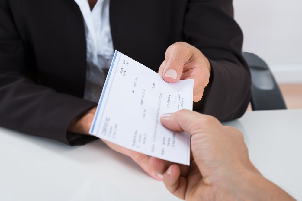 Un superior en el lugar de trabajo entregando un cheque de pago a un empleado.