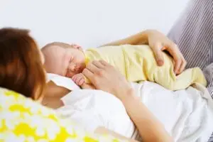 Baby resting on belly of new mother in bed while on maternity leave