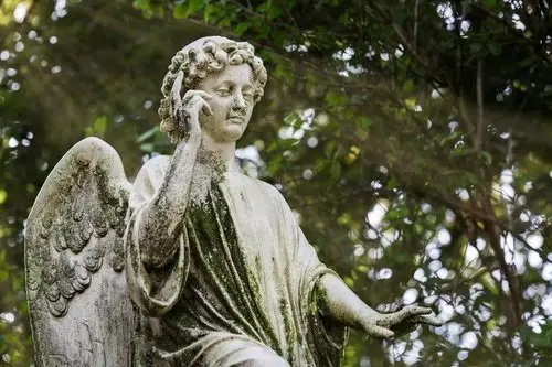 Statue of an angel at a cemetery with trees in the background