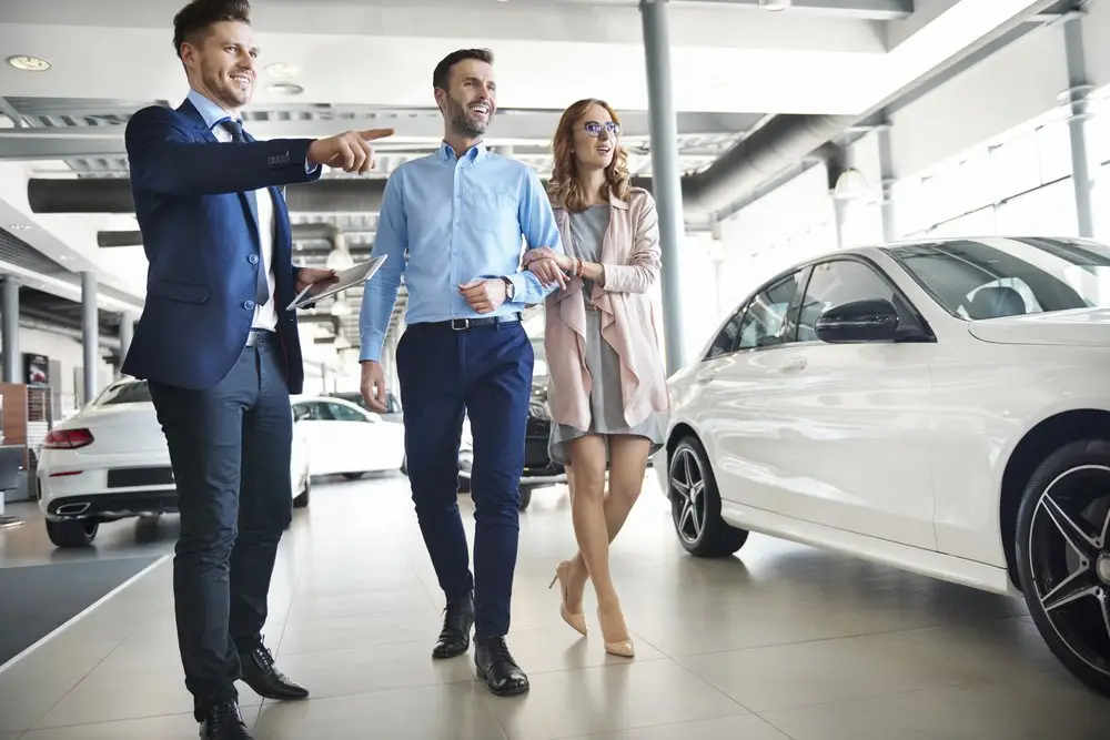 A car salesman in a business suit showing an excited young couple a new car in a show room