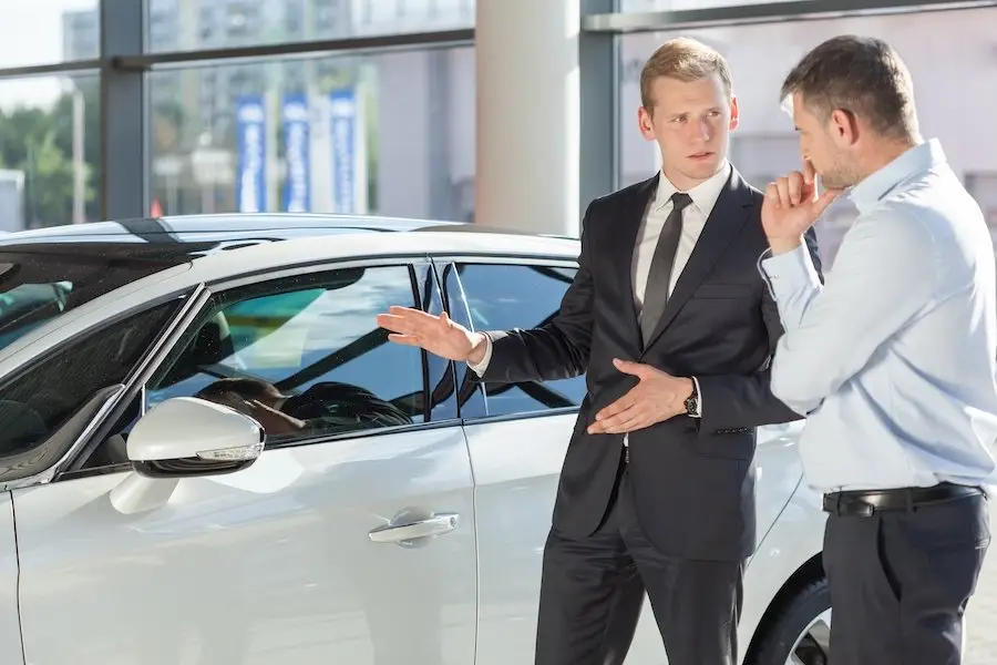 Car salesman in a business suit with customer in front of white sedan in a showroom