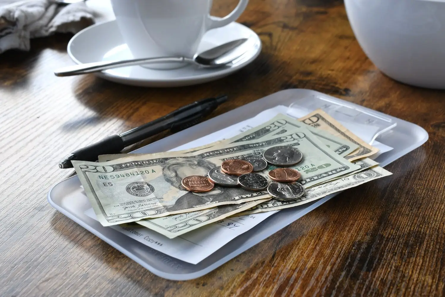 Cash and coins left as a tip at a restaurant table next to a cup of coffee