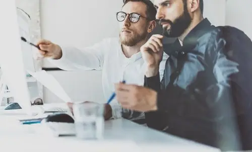 Two computer professionals looking at a computer screen on a white desk in an office