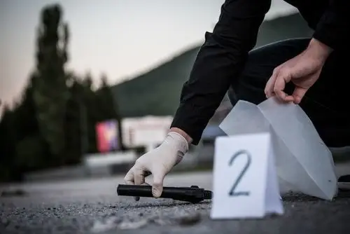 Forensic officer at a crime scene collecting a gun with a gloved hand to put in an evidence bag