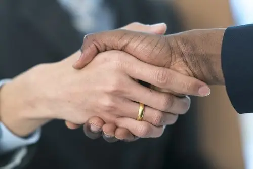 An office worker shaking hands with a boss, and the office worker's hand has a wedding ring