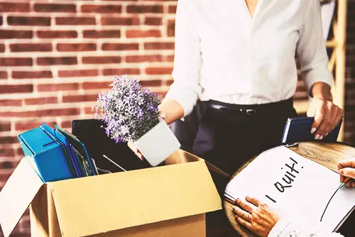 employee quitting and putting away her belongings in a cardboard box, and he is standing in front of a brick wall