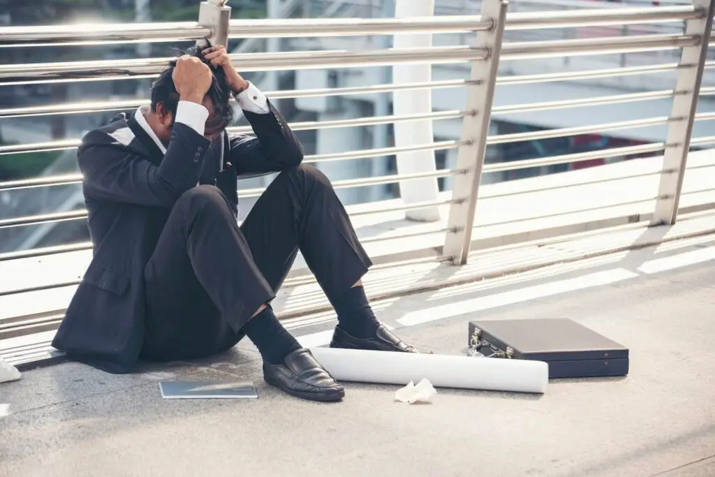 Fired employee in business suit holding his head in despair on floor next to his briefs case and crumpled documents