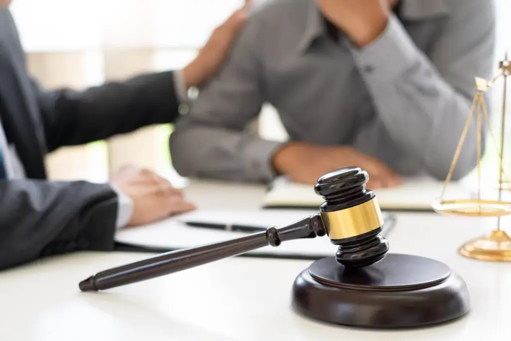 Attorney comforting client with gavel and a scale of justice in the foreground