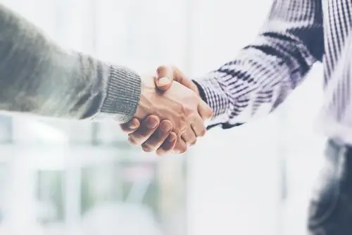 close-up of a new employee and employer shaking hands against a blurry background in an office after they sign an employment agreement with a severance package