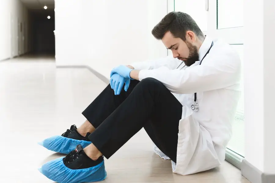 Tired hospital staffer taking a nap while sitting against the wall in a hospital hallway
