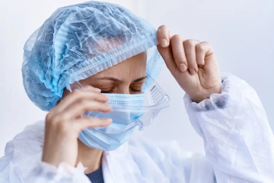 Tired hospital staff worker taking off her hair net and face mask