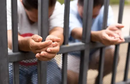Crouching immigrants in a detention jail with their hands extended out of the cell bars