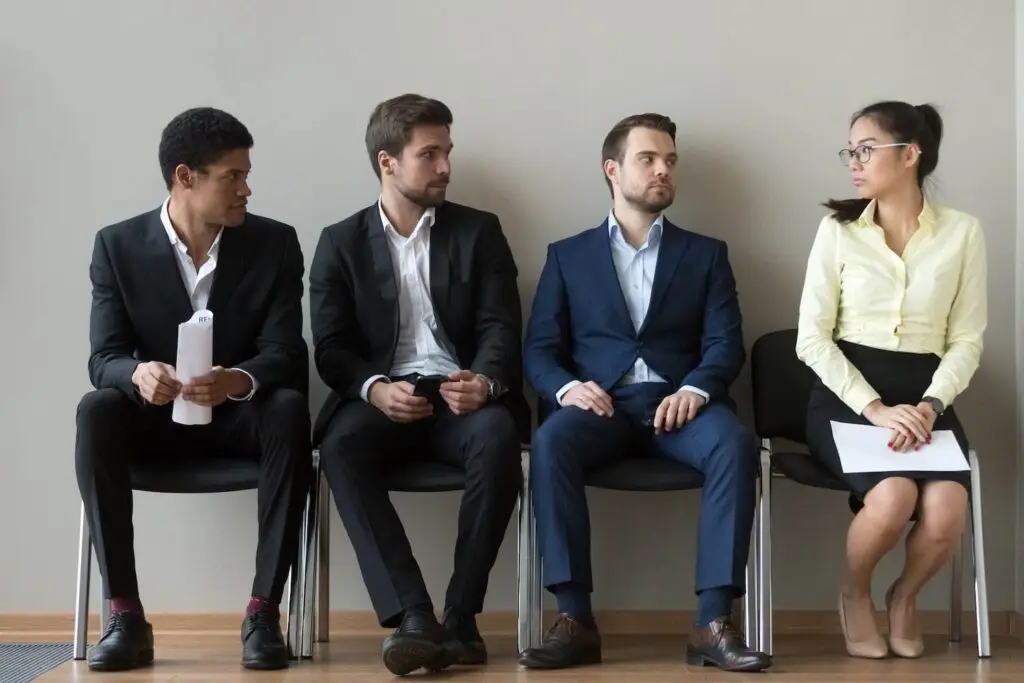 Three male employees looking suspiciously at female employee while they are waiting for a job interview
