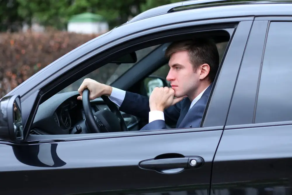 Pensive-looking man in a business suit driving his black sedan on a work trip