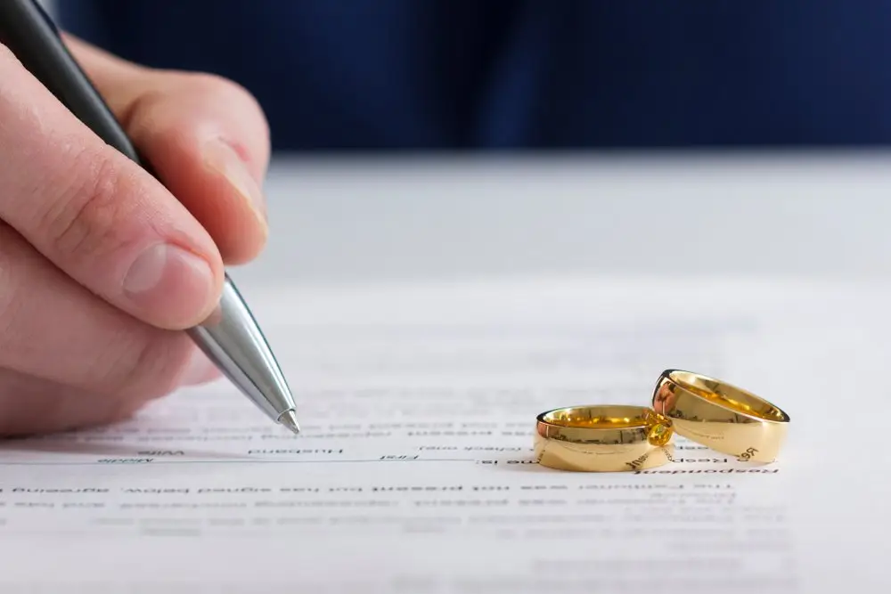 A person writing down his marital status on a form with two gold wedding rings on the paper