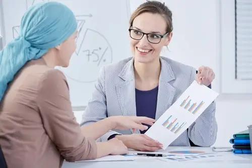 Two co-workers discussing work charts, and one of them is wearing a head scarf, indicating she is undergoing chemotherapy