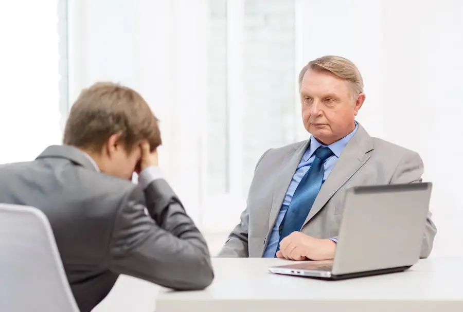 Employer by his laptop on his desk looking at distraught employee who was just terminated