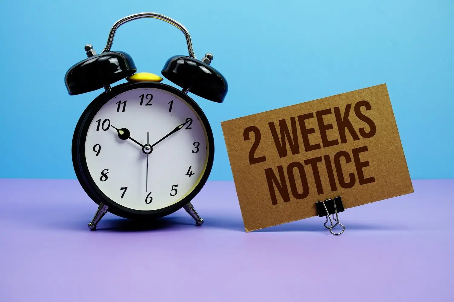 Alarm clock next to a sign that says 2 weeks notice
