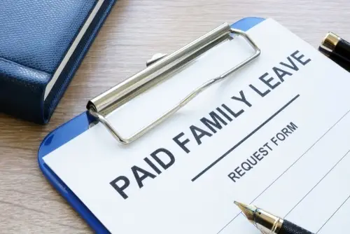 On a desk, a clipboard holding paper that says, "Paid Family Leave Request Form" with a pen resting on it