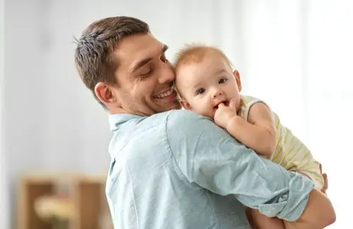 New father holding his baby in his arms in his living room while on paternity leave