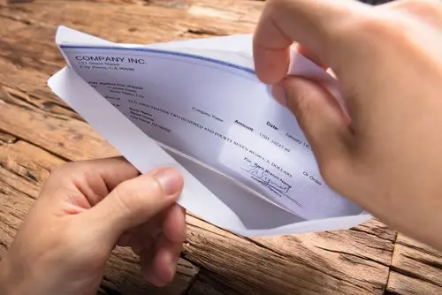 Close-up of hands opening an envelope with a paycheck inside, with a wooden table underneath