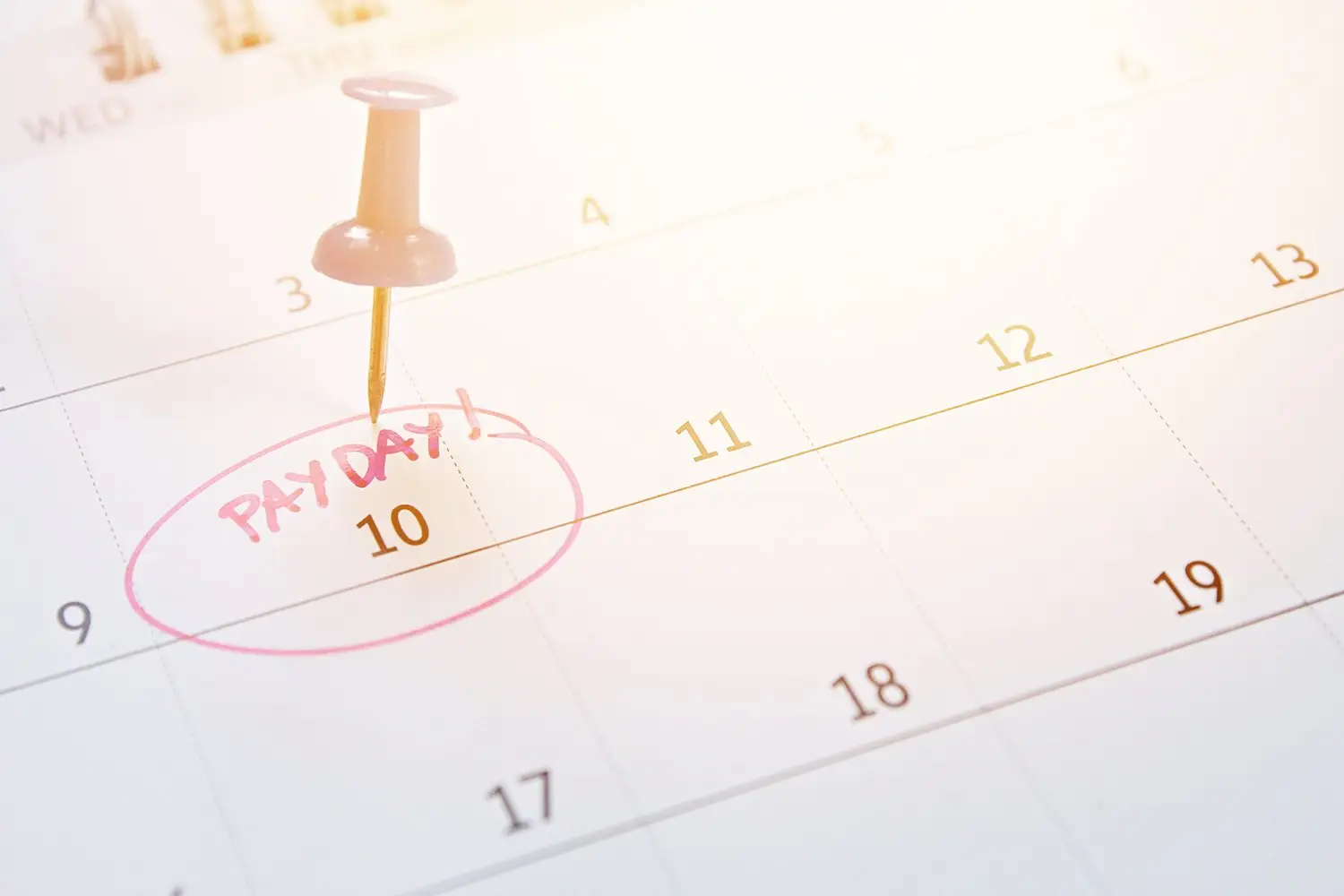 Calendar that says "payday" on the 10th with the date circled and a pin stuck in it