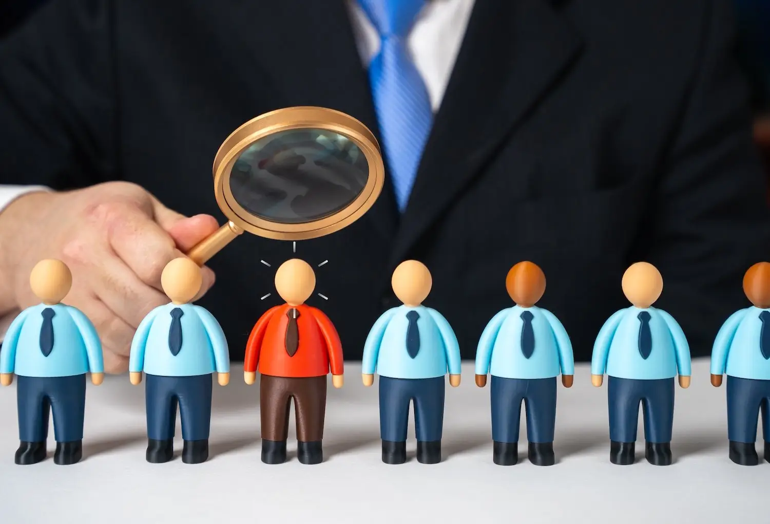Magnifying glass over dolls of employees to signify a workplace investigation 