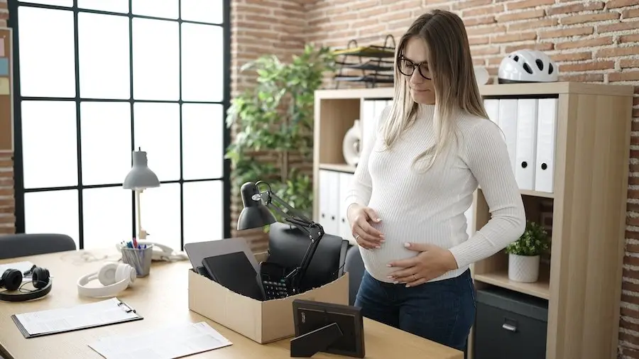 Sad-looking pregnant woman in a business office packing up her desk after getting fired