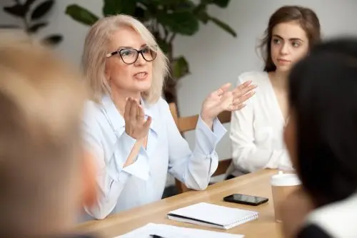 an attorney, who is professionally exempt under California labor law, is speaking with employees during an office meeting at a board table