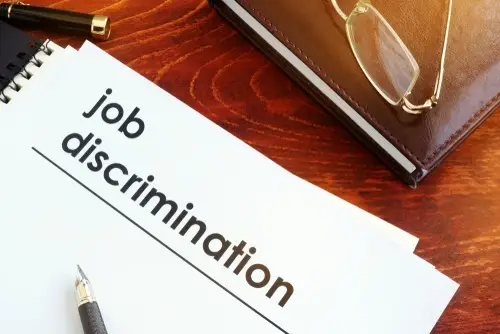 Binder with front page titled "job discrimination." It is resting on a wooden table next to a leather-bound folder, a pen, and glasses