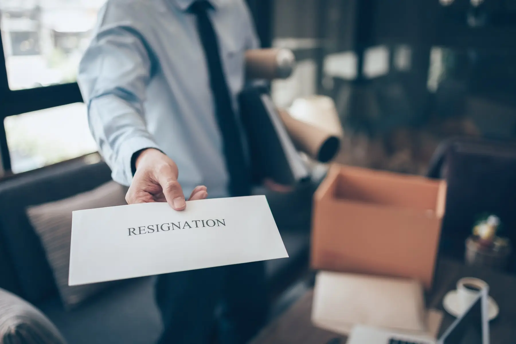 Office worker handing an envelope titled "resignation" on it to the boss behind the camera