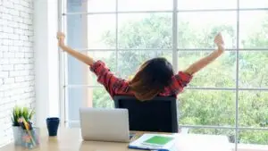 Woman at desk stretching during a rest break from work while looking out her office window