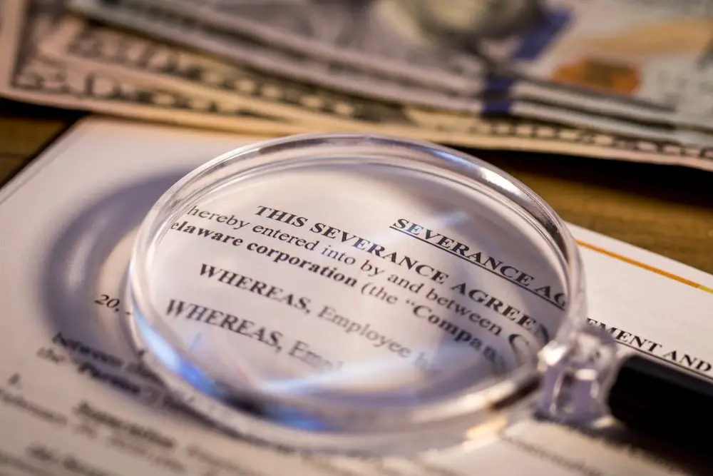 A severance agreement with a magnifying glass resting on it and with cash in the background