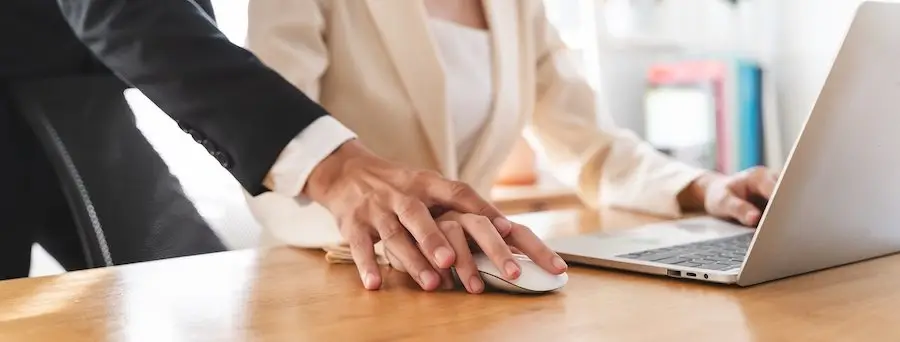Close-up of a boss's hand touching an employee's hand over a computer mouse in an act of sexual harassment. 