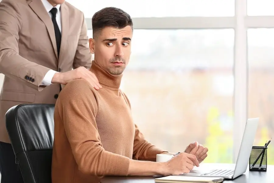 Male boss putting his hands on the shoulders of a male employee in an act of sexual harassmenet