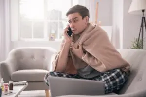 Sick employee at home on phone in front of laptop