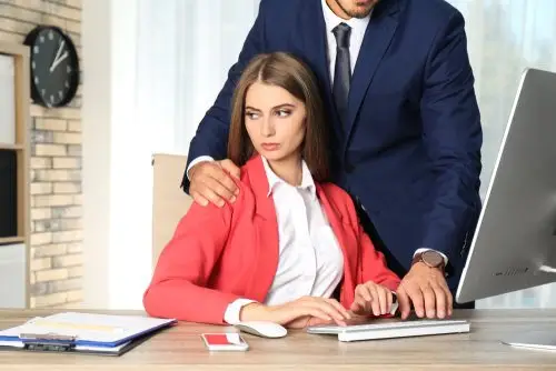 Seated woman at her work computer being touched on her shoulder by a standing male co-worker