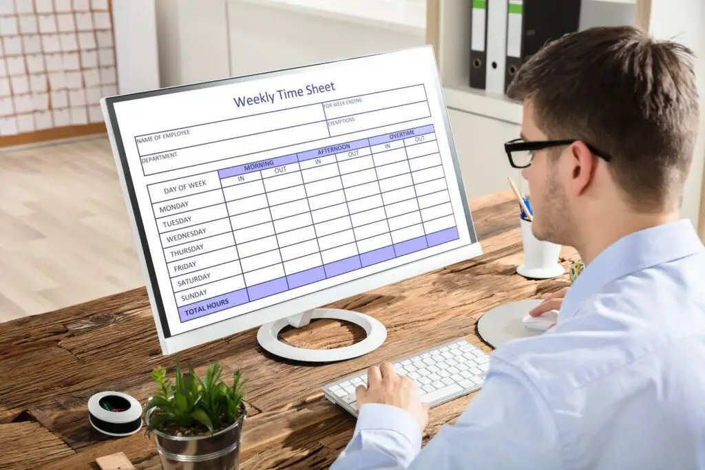 Worker filling out timesheet on computer at his office desk