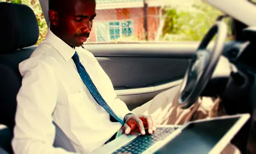 man in shirt and tie working a laptop while in the driver's seat of a vehicle as an example of when the California outside sales exemption may apply