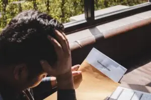 Worker holding his head in one hand and a termination letter in the other hand by a window