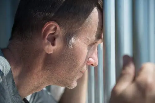 Older gentleman inmate in his cell holding the cell bars while looking through them
