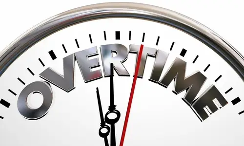 Portion of a a white and silver clock that reads "Overtime" against a white background