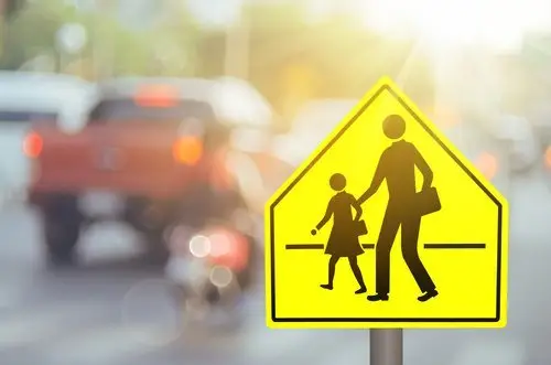 Yellow school crossing street sign against a blurry background of a city street