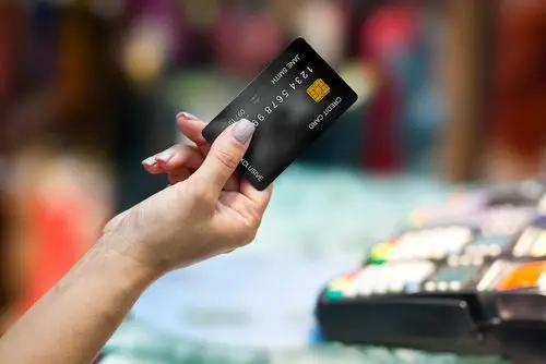 Close-up of hand holding out a black credit card with a cash register in the background