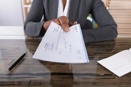 Close-up of boss in a business suit handing check to employee over a glass desk
