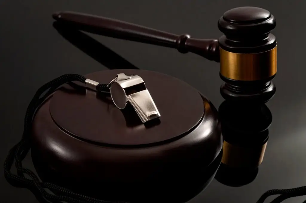Wooden judge's gavel next to a silver whistle on a dark desk