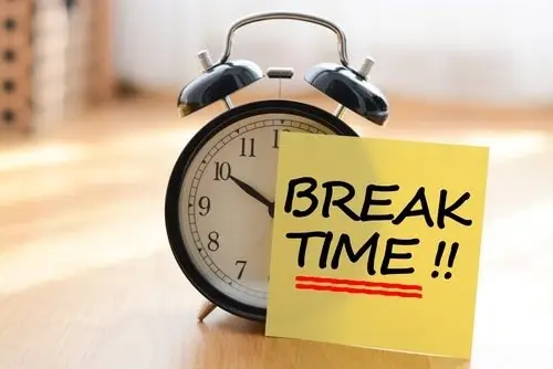 Alarm clock with yellow post-it note that reads "Break Time!!", resting on a wooden floor