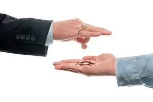Hand of boss dropping pennies in hand of underpaid worker